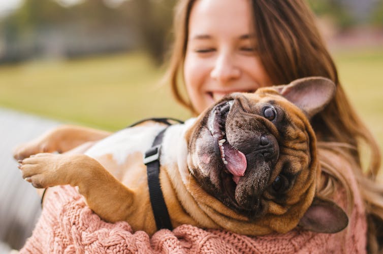 A smiling woman carries a bulldog